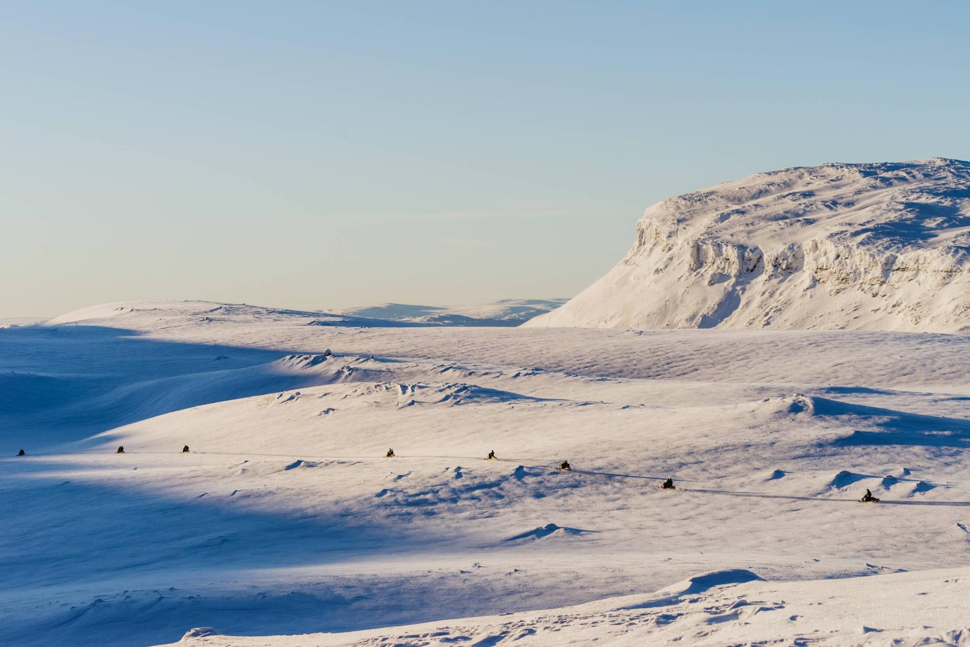 Snowmobiles crossing open snow below a flat-topped fell in Finnish Lapland