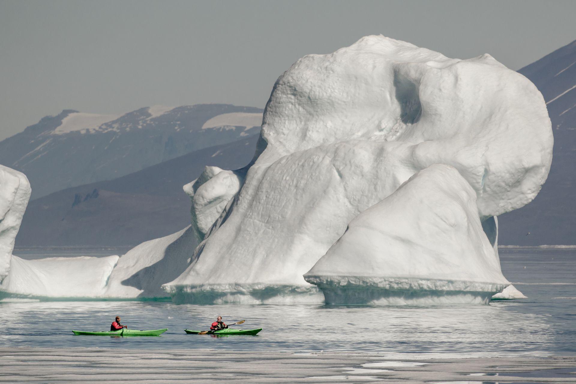 Kayakers paddling beside an iceberg in North Greenland